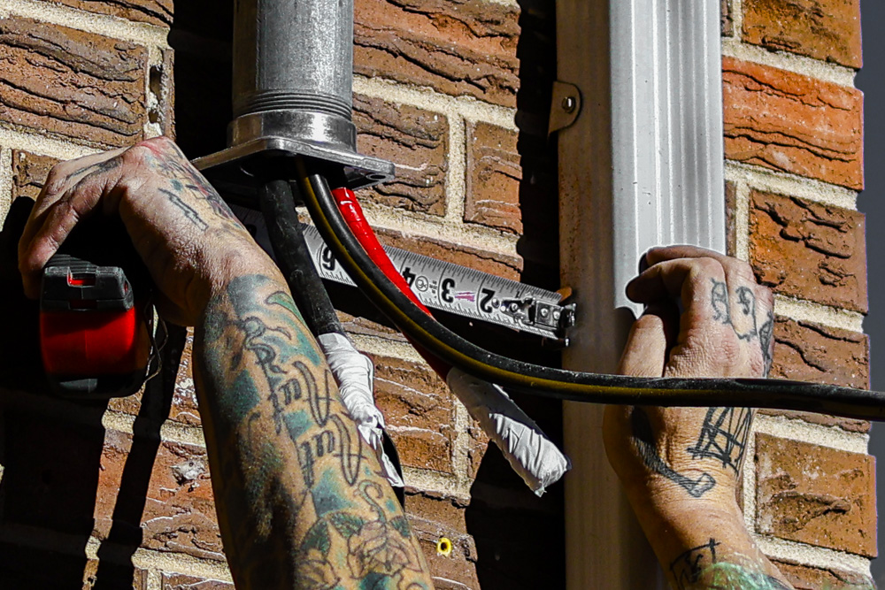 Tattooed hands running conduit on brick exterior